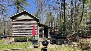 A log cabin with a patio area, a grill, and a hot tub.