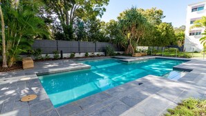Una piscina rettangolare con bordo piastrellato, immersa nel verde e circondata da una recinzione in legno.