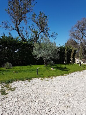 Un chemin de gravier mène à une zone herbeuse, avec des arbres et un mur de pierre en arrière-plan.