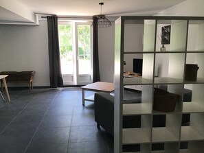 Un salon moderne avec un canapé, une table et un téléviseur. Il y a une grande fenêtre avec des rideaux, un luminaire au plafond et une bibliothèque.