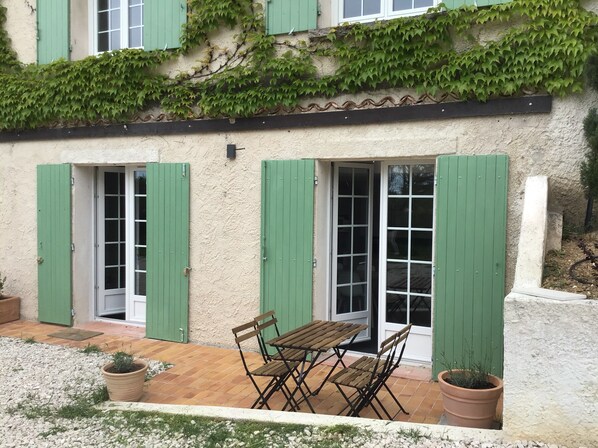 Un bâtiment rustique avec des volets verts, une table et des chaises en bois, et des plantes en pot.