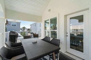 A covered patio with a table and chairs, a sliding glass door, and a view of neighboring houses. - Casa Mimosa: Your Private Beach Escape with Pool, Bikes & Steps to the Sand (Santa Rosa Beach)
