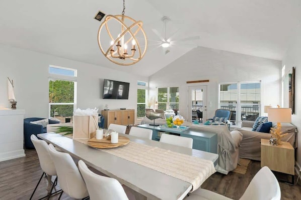 A spacious living area with a dining table, seating, a chandelier, and a television.