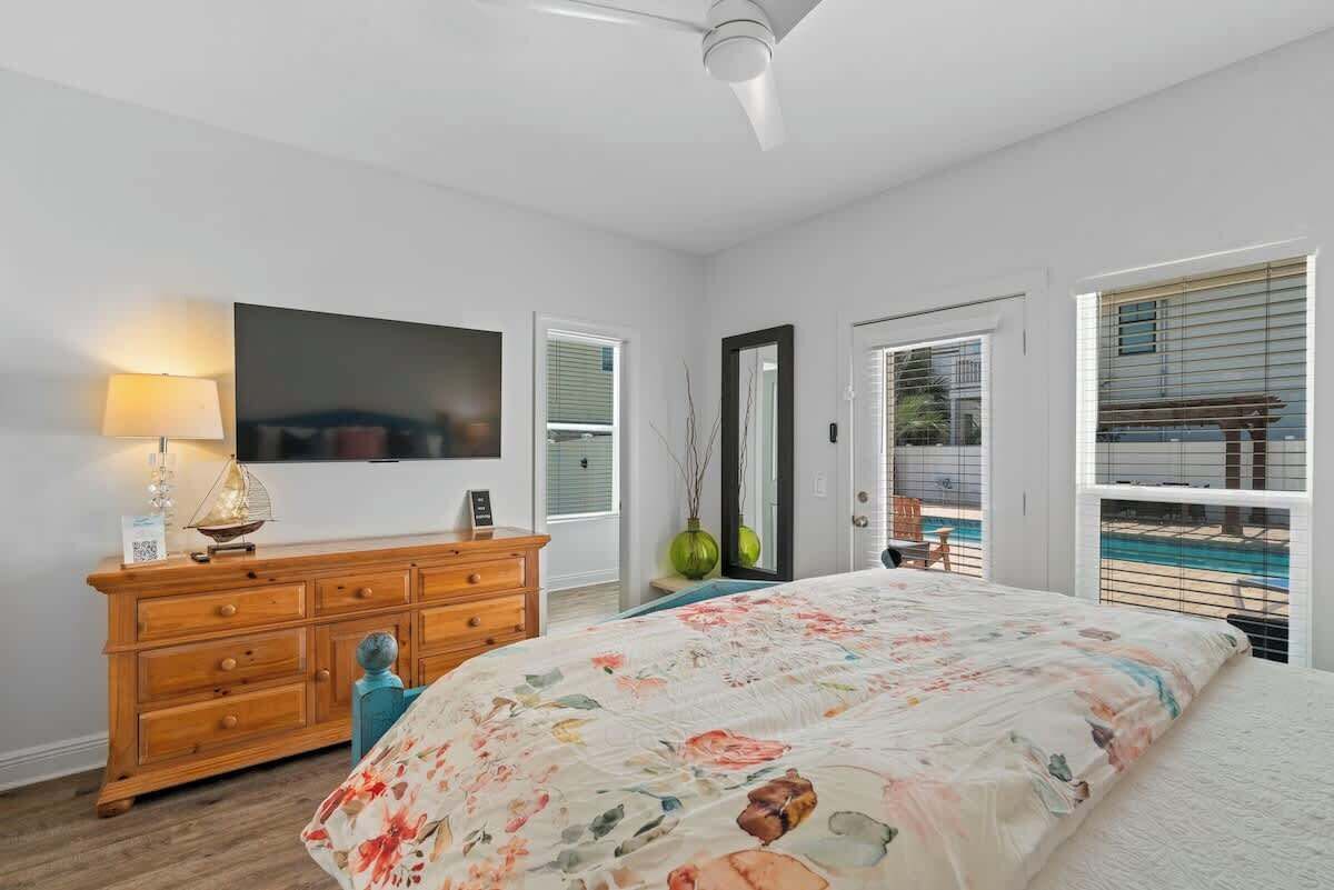 A bedroom with a bed, dresser, lamp, mirror, and windows.