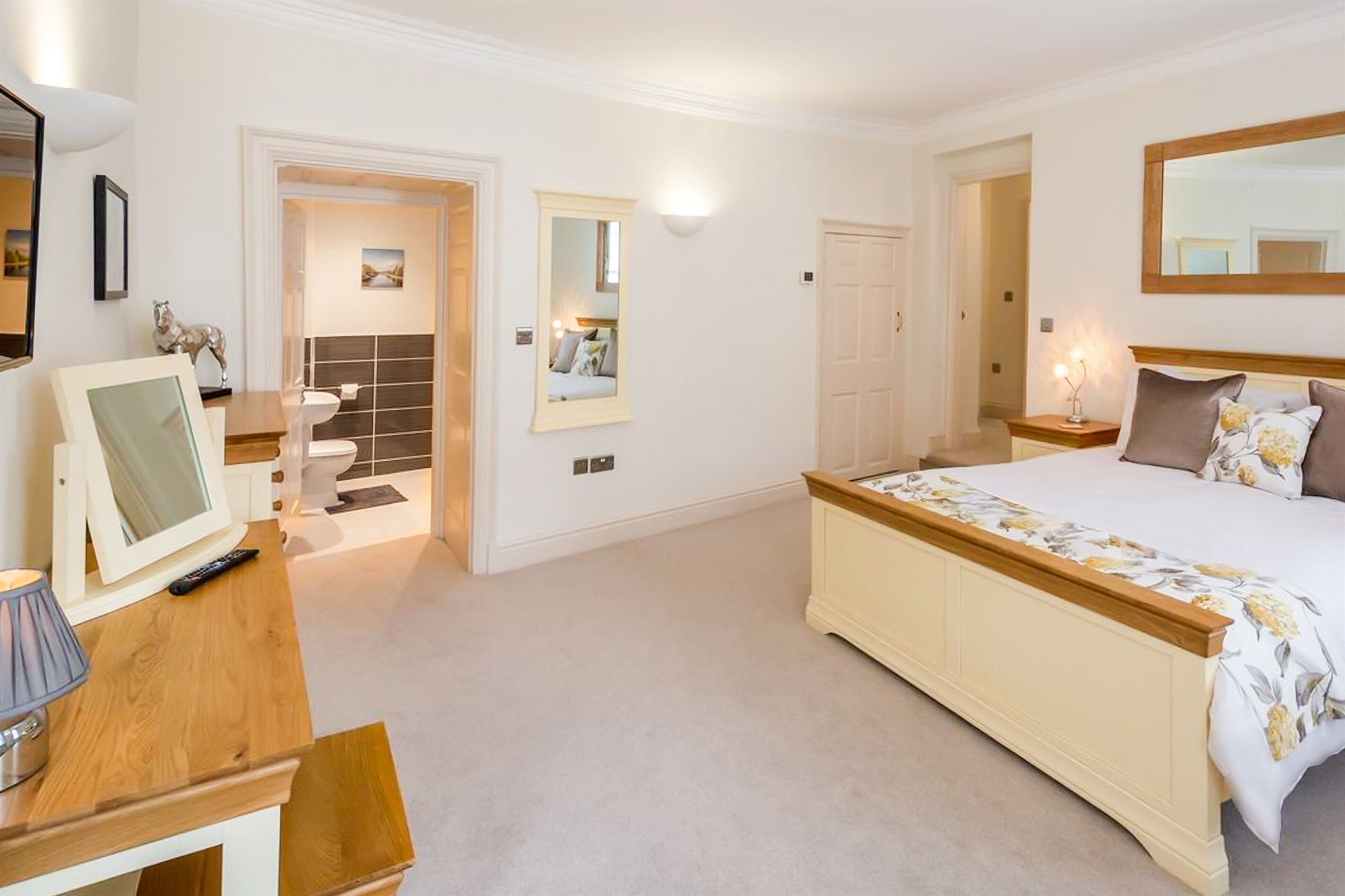 A bedroom with a large bed, a bedside table, a mirror, and a door leading to a bathroom.