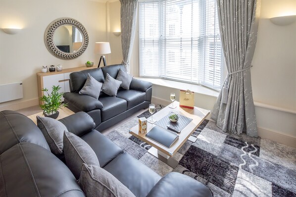 A modern living room with a black leather sofa, a coffee table, and a potted plant.