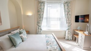 Une chambre à coucher avec un lit, un bureau, une télévision et une fenêtre avec des rideaux.