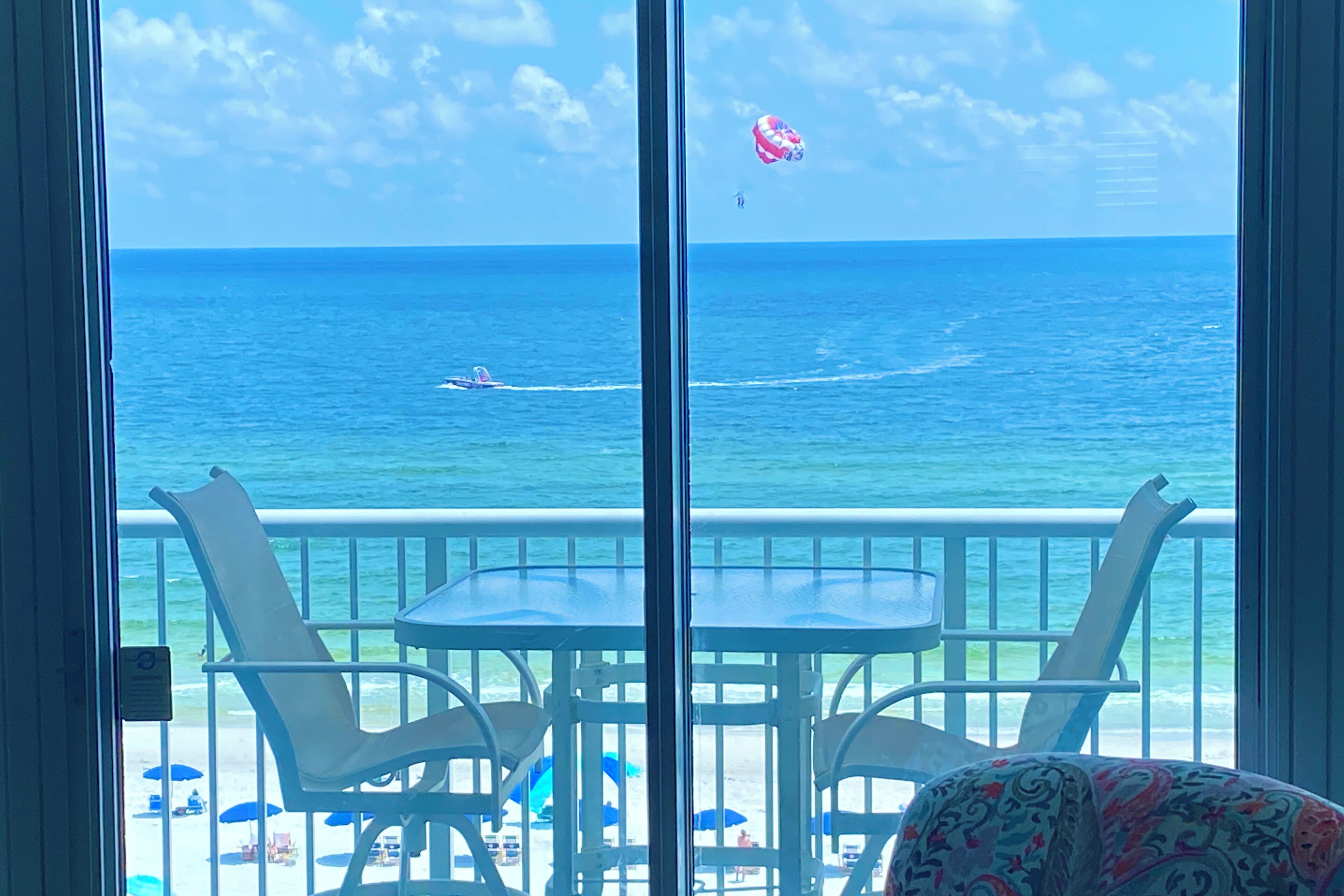 Ein Balkon mit Meerblick, ausgestattet mit einem Tisch und Stühlen, und ein Strand mit Sonnenschirmen und Liegestühlen.