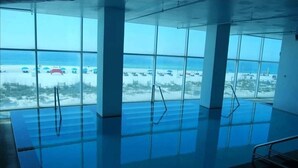 A swimming pool with clear views of the beach and ocean through large windows. - Serenity: Island Tower 702 3BR 3BA, 2 Gulf-Front Masters, + Free Beach Service!! (Gulf Shores)