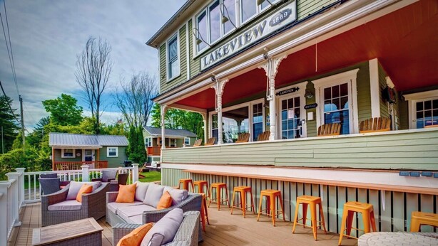 Un bar situé au bord de l’eau, avec des meubles et des tabourets en osier, un espace de repos couvert et une enseigne indiquant « LAKEVIEW 1869 ».