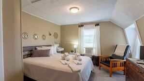 Une chambre à coucher comprenant un lit, une table de chevet, une chaise, une commode et une fenêtre avec des rideaux.
