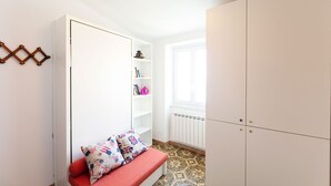 A room with a red sofa, white wardrobe, and a white shelving unit against a white wall.