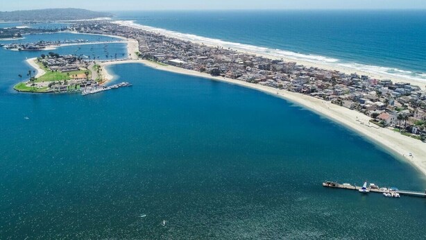 Vista aérea de una ciudad costera con un puerto deportivo, una playa y una península con edificios.