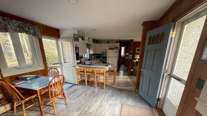 A compact kitchen with wooden cabinets, a dining table with chairs, and a large window providing natural light. - South Chatham cottage walk to beaches, dining, tennis, shops, bike path.  (Chatham)
