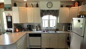 A kitchen with white cabinets, a dishwasher, a sink, a refrigerator, and a window with a floral curtain. - South Chatham cottage walk to beaches, dining, tennis, shops, bike path.  (Chatham)