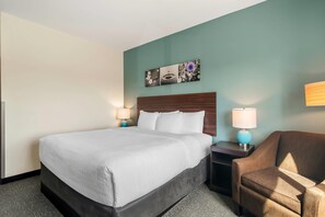 A hotel room with a large bed, two bedside tables with lamps, a brown armchair, and a wall-mounted picture. - Sleep Inn & Suites Webb City (Webb City)