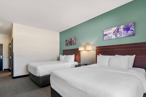 Habitación de hotel con dos camas, cabecera de madera, mesita de noche y obra de arte colgada en la pared.
