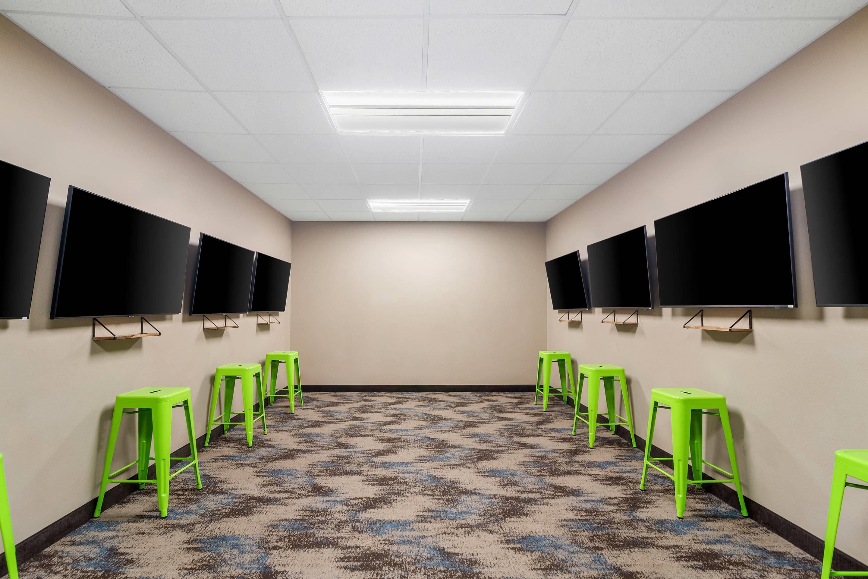 A conference room with a patterned carpet, green stools, and multiple black screens on the walls.