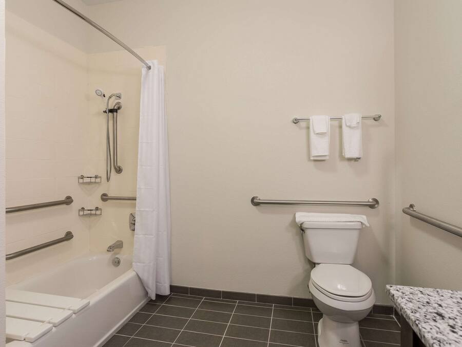 A bathroom with a bathtub, toilet, grab bars, and a shower curtain.