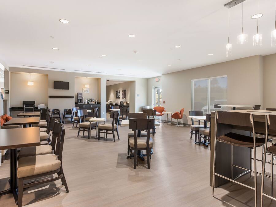 A modern hotel lobby with multiple seating areas, a coffee station, and a visible kitchen area.