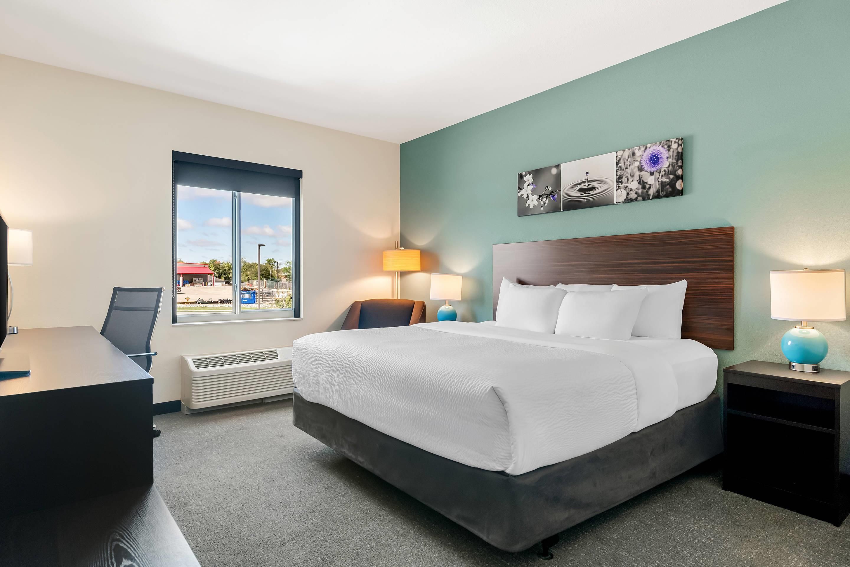 A hotel room with a bed, bedside tables, a desk, a chair, a window, and a wall-mounted artwork.