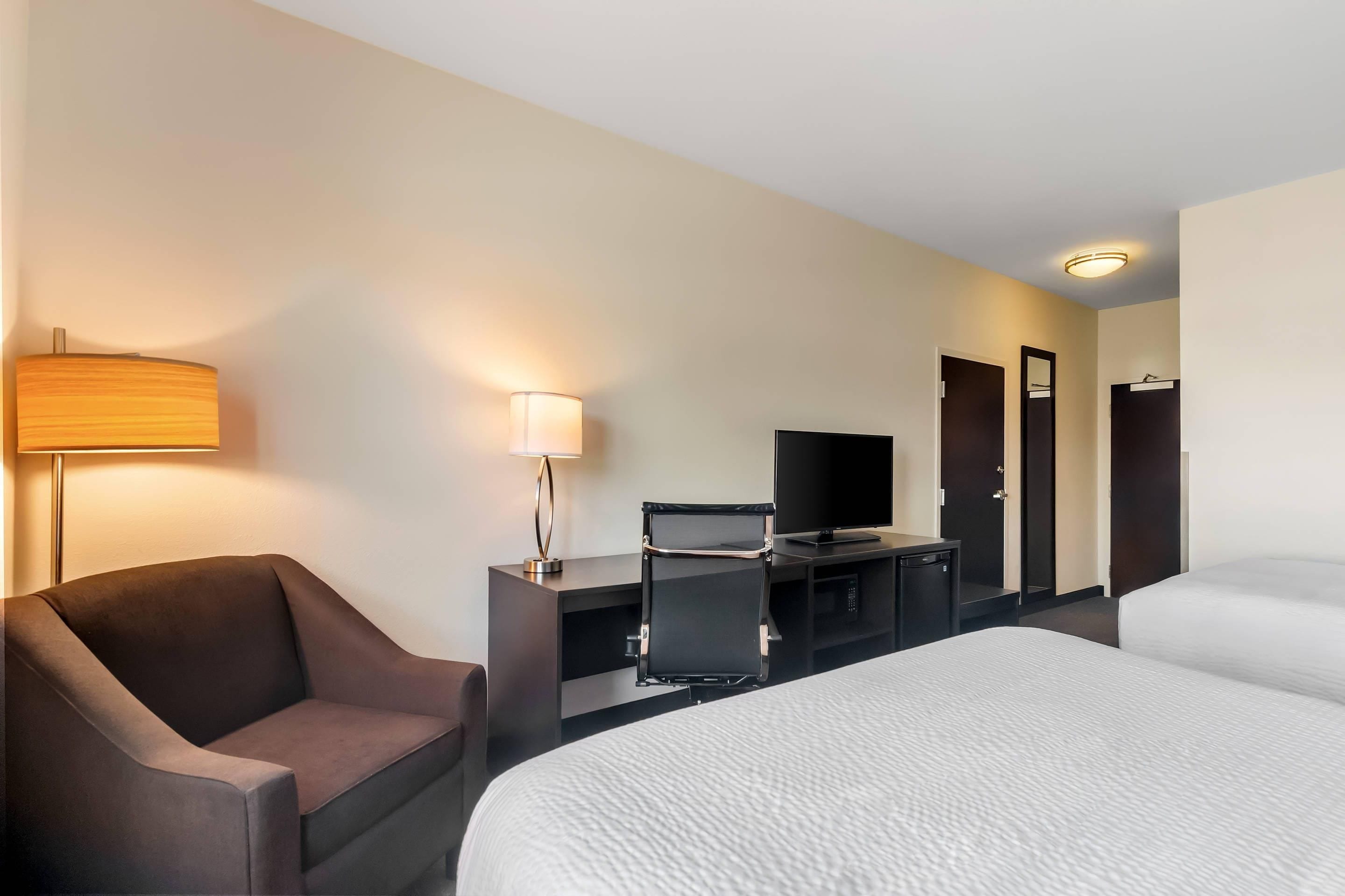 A hotel room with a bed, a desk with a computer, a TV, a chair, and a lamp.
