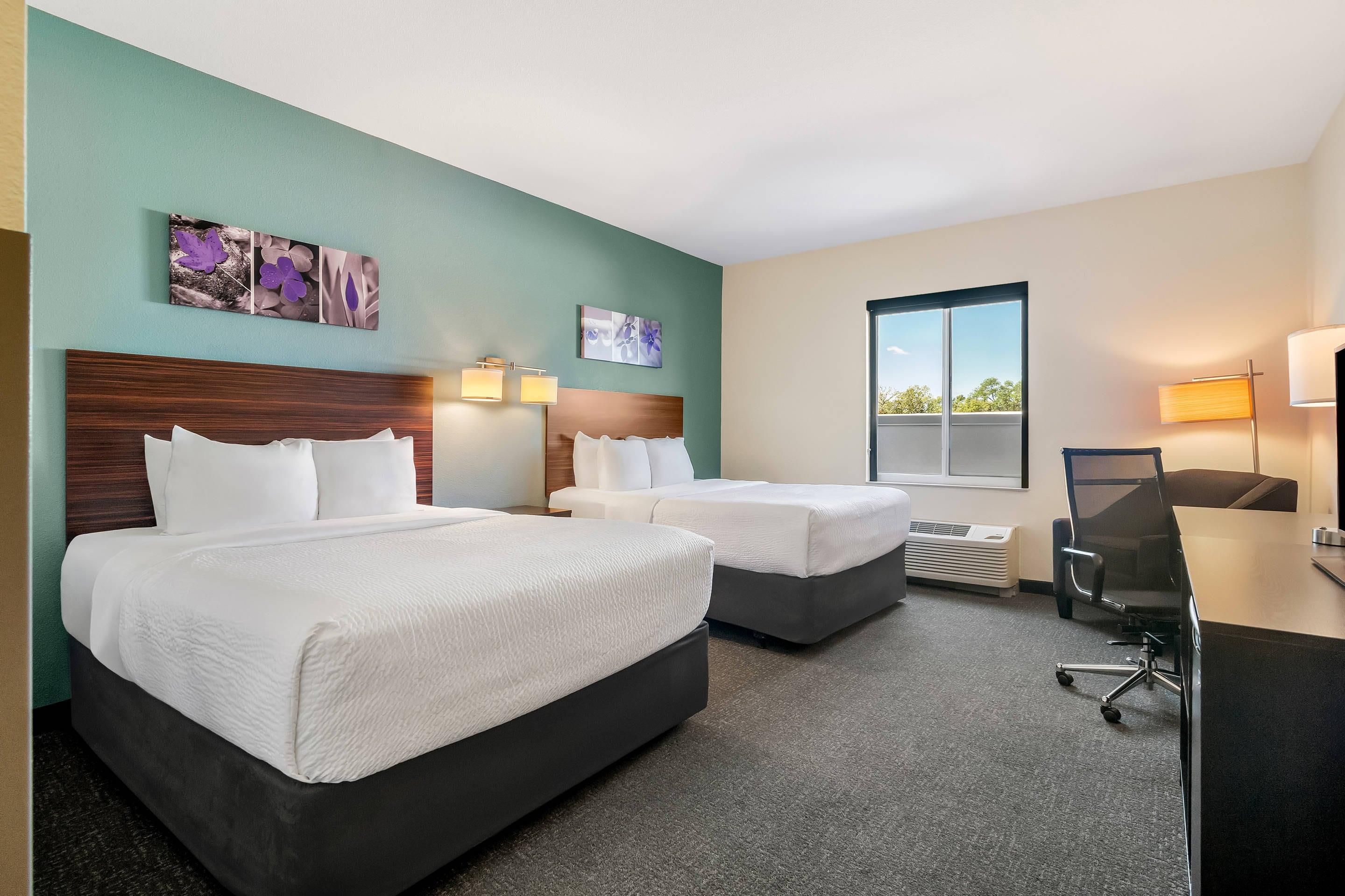 A hotel room with two beds, a desk, a chair, and a window.