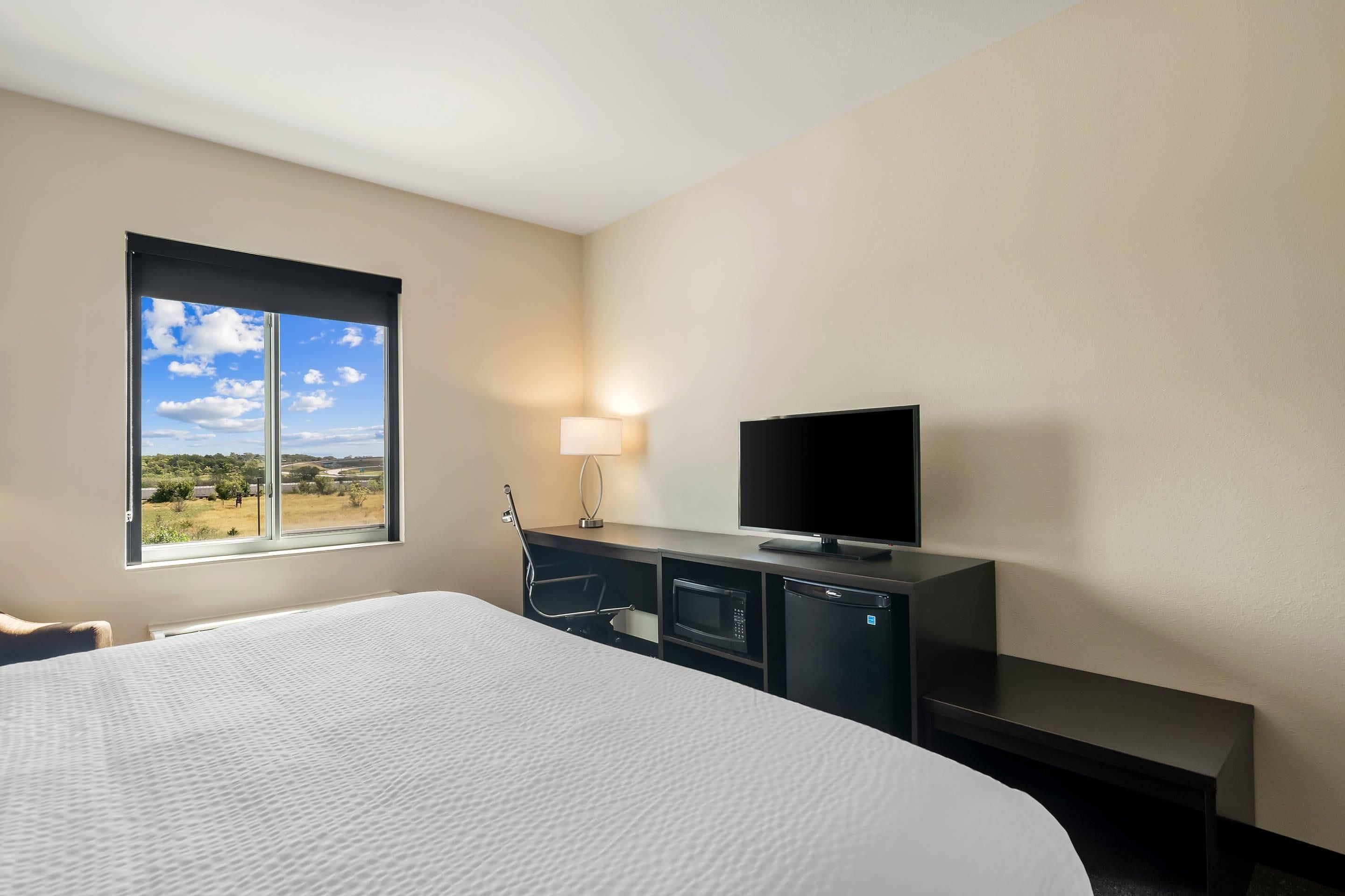 Habitación de hotel con una cama grande, un televisor de pantalla plana, un escritorio con lámpara y vistas al exterior.