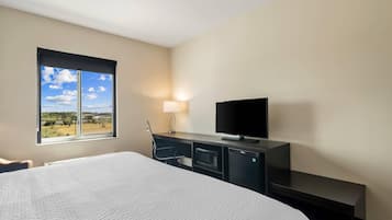 Habitación de hotel con una cama grande, un televisor de pantalla plana, un escritorio con lámpara y vistas al exterior.