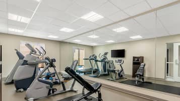 Une salle de sport équipée de matériel d’exercice, d’un miroir et d’un téléviseur.
