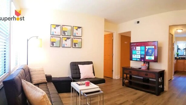 Una sala de estar con un sofá, una mesita, un televisor y obras de arte enmarcadas en la pared.