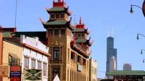 Un edificio tradicional con varios niveles y techos rojos, situado en una zona urbana con rascacielos modernos al fondo.