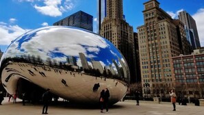 Una esfera metálica grande que refleja el paisaje urbano, rodeada de edificios altos.
