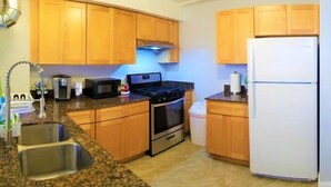 Una cocina con armarios de madera, un lavamanos de acero inoxidable, una estufa, un microondas y un refrigerador.