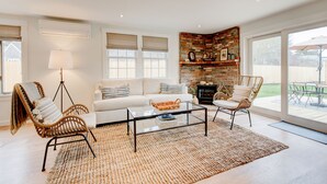 Ein modernes Wohnzimmer mit einem weißen Sofa, Korbstühlen, einem Glastisch und einem Kamin aus Backstein.