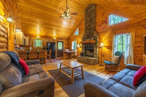 A log cabin interior with a fireplace, wooden furniture, and a stone accent wall. - Leaning Tree - Cozy Log Cabin in the Hocking Hills (Logan)