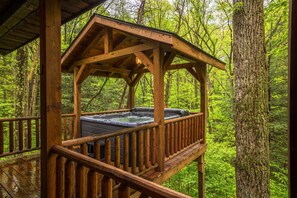 Un bain à remous en bois, installé sur une terrasse en bois, entouré d’une forêt.