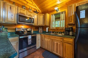 A wooden cabin kitchen with a microwave, stove, oven, and refrigerator. - Leaning Tree - Cozy Log Cabin in the Hocking Hills (Logan)