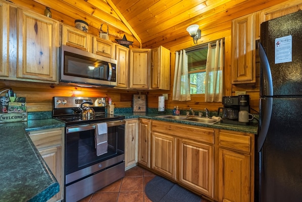 A wooden cabin kitchen with a microwave, stove, oven, and refrigerator. - Leaning Tree - Cozy Log Cabin in the Hocking Hills (Logan)