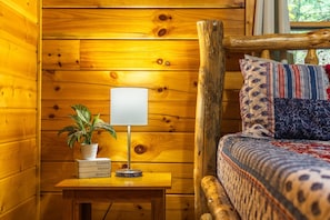 L’intérieur d’un chalet en bois, avec un lit, une table de chevet dotée d’une lampe, une plante en pot et une fenêtre avec des rideaux.