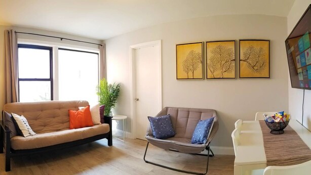 A living room with a sofa, a chair, a small table with a bowl of snacks, and three framed artworks on the wall. - 1 #23 - 4 Bedroom Condo - McCormick Place, Wintrust Arena, Chinatown (Chicago)
