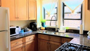 A kitchen with wooden cabinets, a gas stove, a microwave, a coffee maker, and a window with curtains. - 1 #23 - 4 Bedroom Condo - McCormick Place, Wintrust Arena, Chinatown (Chicago)