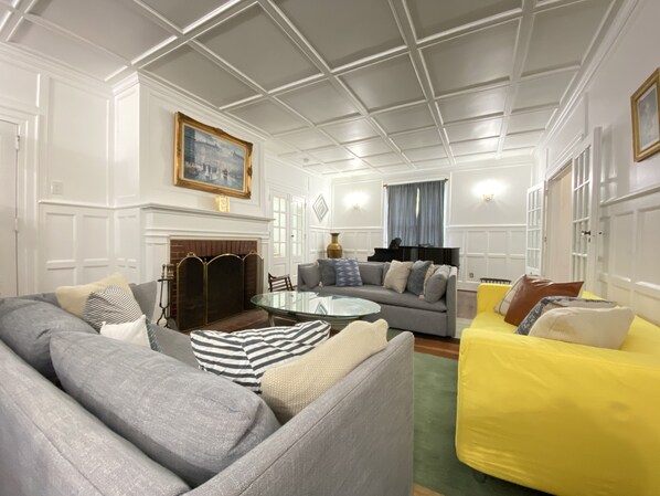 Ein Wohnzimmer mit Kamin, Klavier und einem gelben Sofa.