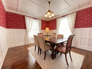 Ein Esszimmer mit Holztisch, vier Stühlen, einer Chandelüster und floralem Wandpapier.