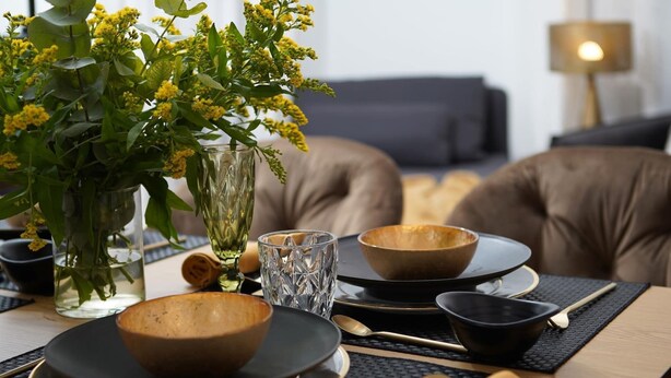 A dining table set with bowls, plates, and cutlery, accompanied by a vase of yellow flowers and a candle. - Duplex Apartment Granada City Centre (Granada)
