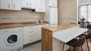 A modern kitchen with white cabinets, a built-in washing machine, a refrigerator, and a wooden countertop. - Duplex Apartment Granada City Centre (Granada)