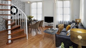 A modern living room with a wooden spiral staircase, a dining area, a sofa set, and a TV. - Duplex Apartment Granada City Centre (Granada)