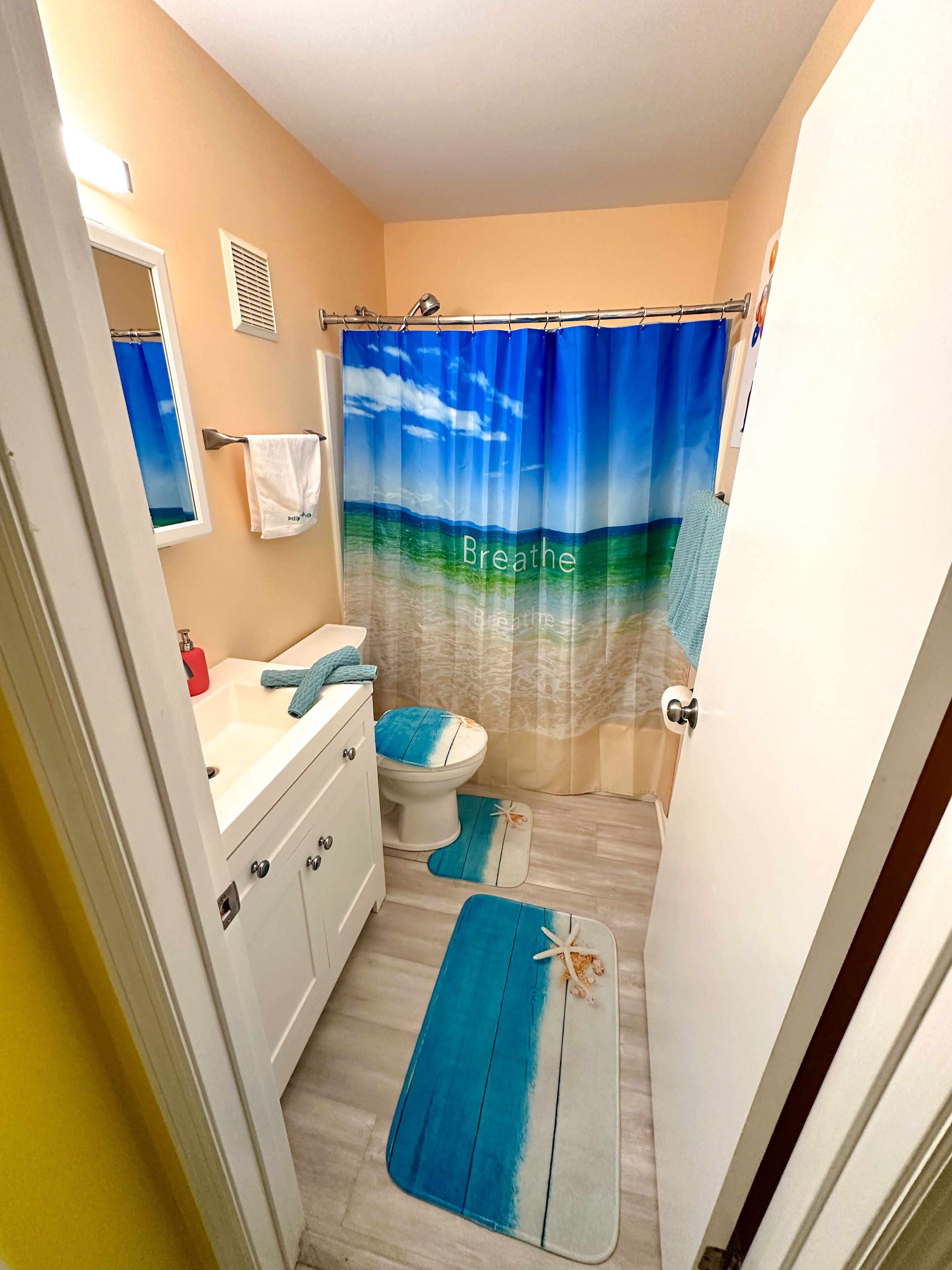 A bathroom with a blue and white ocean-themed shower curtain, a white toilet, and a sink with a towel hanging on the wall.