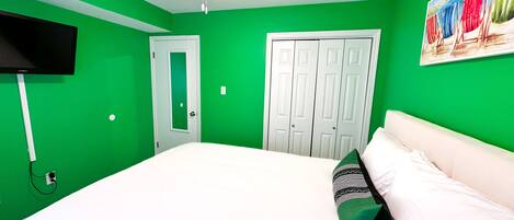 A room with green walls, a ceiling fan, a bed with white bedding, a TV mounted on the wall, and a door with a mirror.