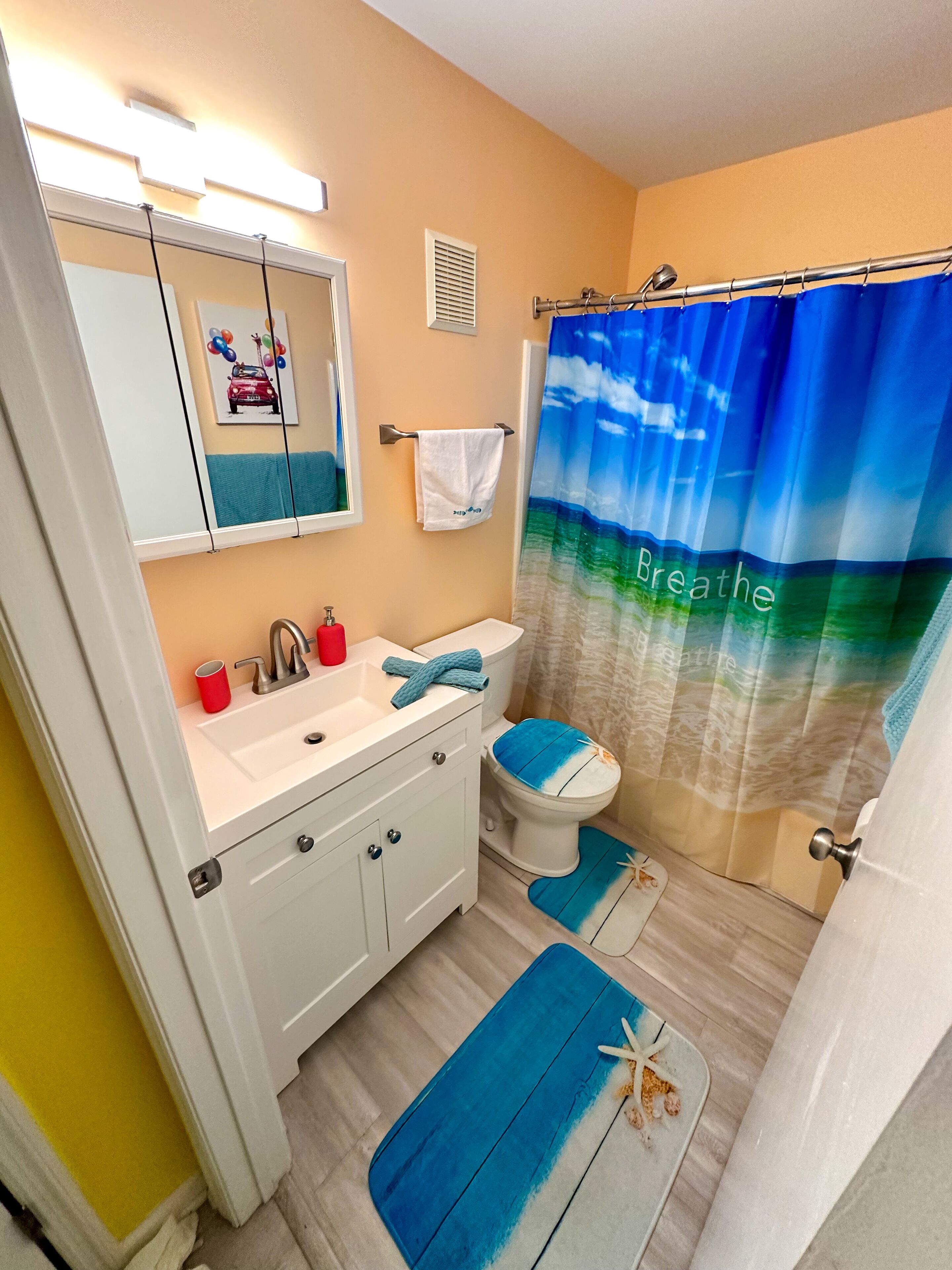 A bathroom with a white sink, mirror, and toilet. There is a blue shower curtain with the word "Breathe" on it.